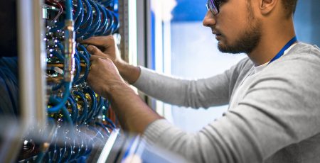 Side view portrait of young man wearing glasses connecting cables in server cabinet while working with supercomputer in data center